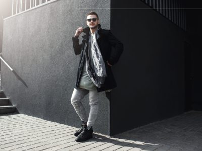 Nice guy in stylish clothing standing outside, leaning to wall. Nice guy in stylish clothing standing outside, leaning to wall, holding phone, looking away.